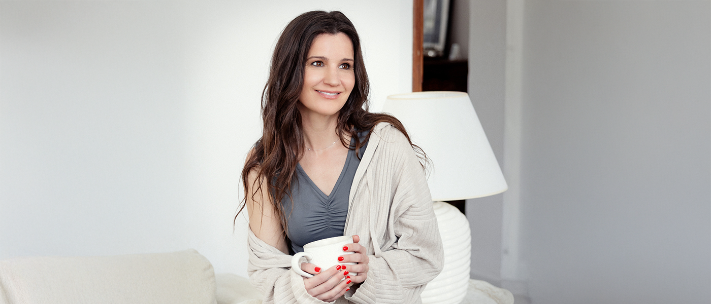 Woman holding a coffee cup, wearing a soft grey Theia Moon tank top with a cozy cardigan: the perfect self-care moment